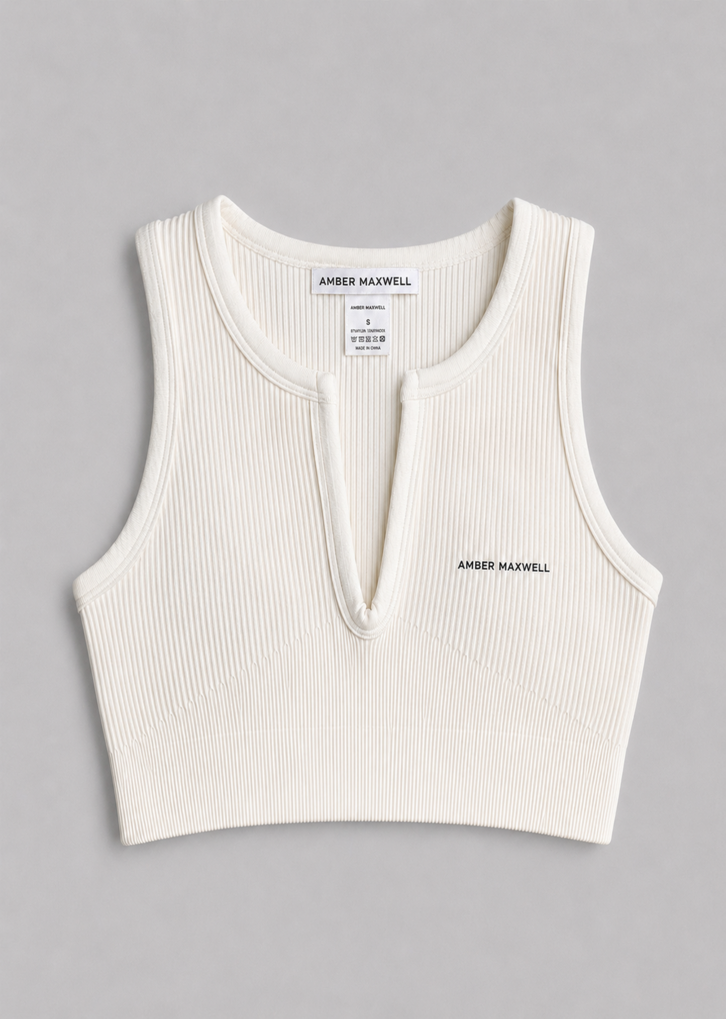 An off-white ribbed knit sleeveless crop top with a split neckline, featuring the brand name 'AMBER MAXWELL' printed on the chest.