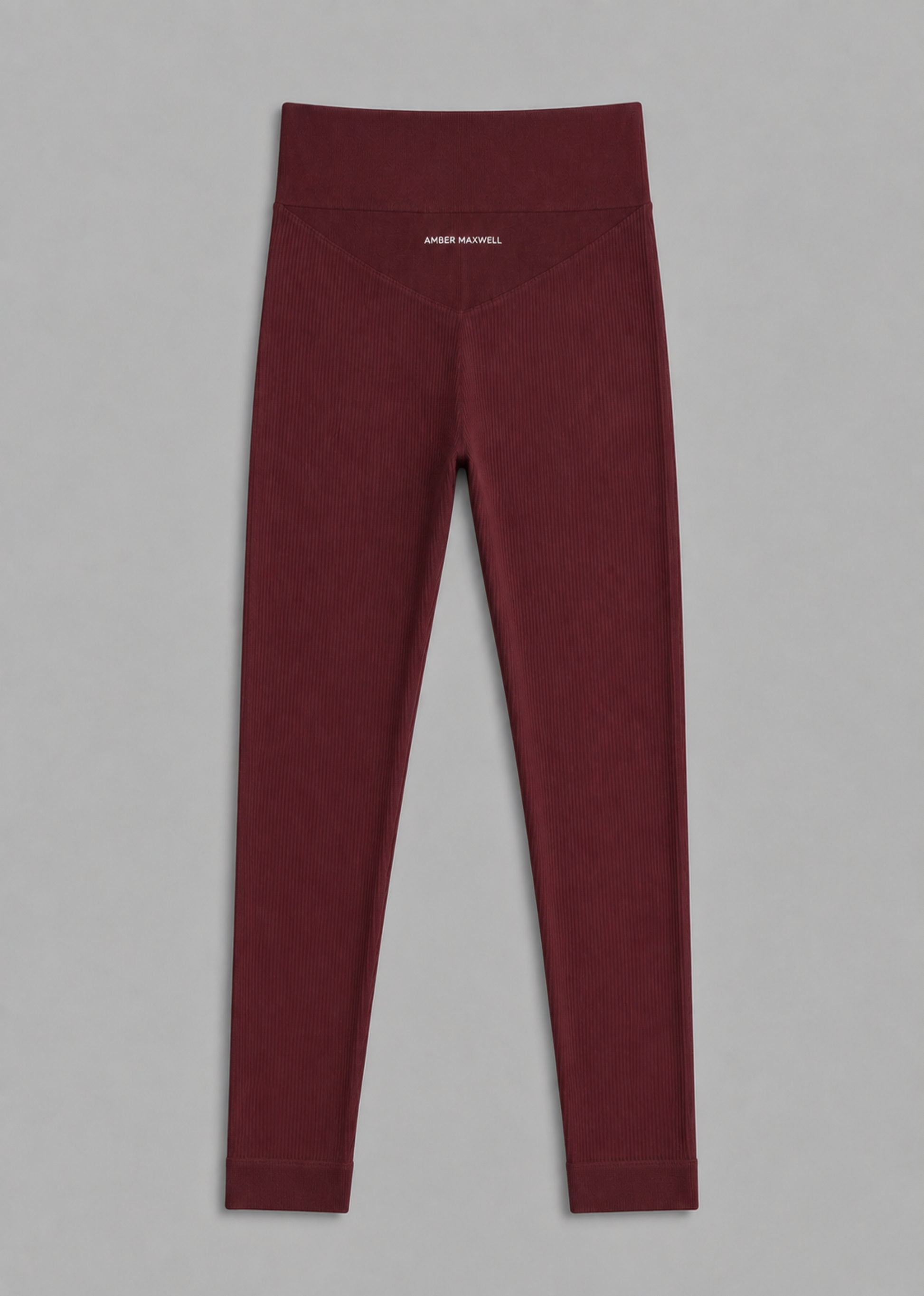 A pair of high-waisted burgundy leggings laid flat on a neutral gray background, featuring a small white embroidered brand logo on the front center waistband.