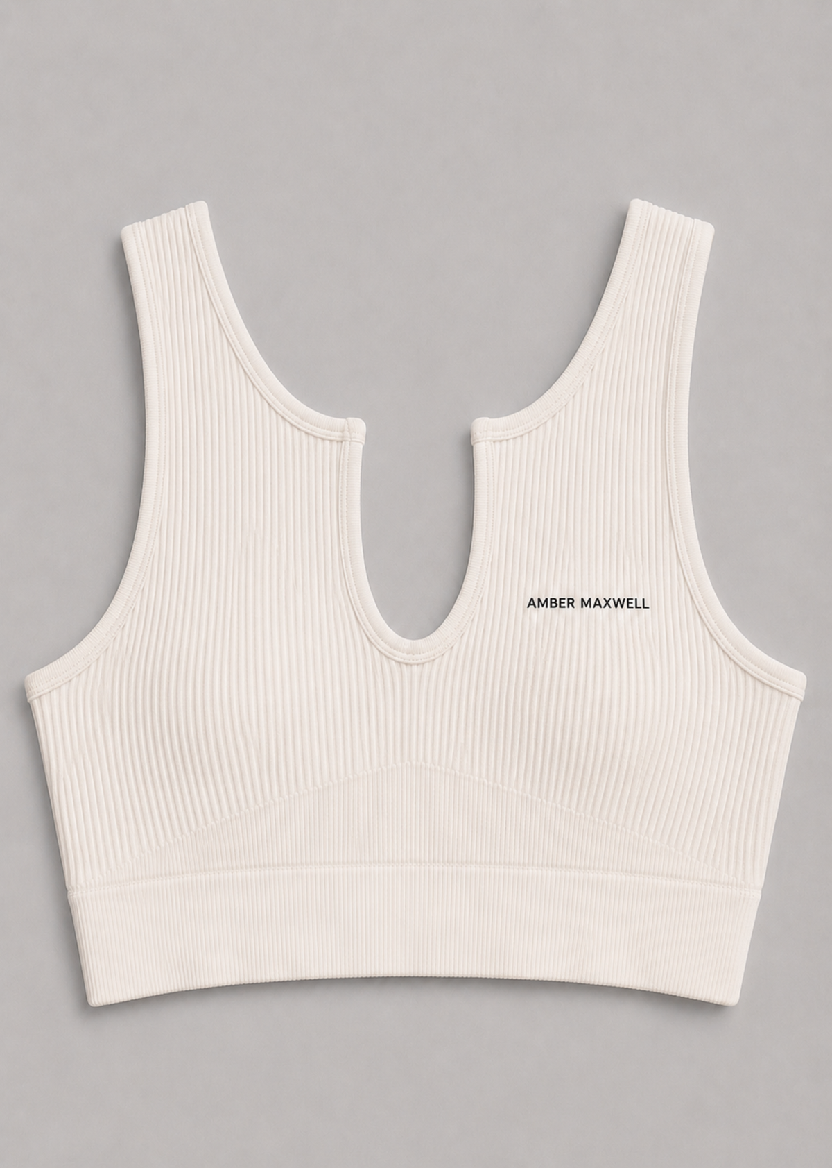 An off-white ribbed knit sports bra with a split neckline and the brand name 'AMBER MAXWELL' printed in black on the left chest, shown flat on a neutral gray background.