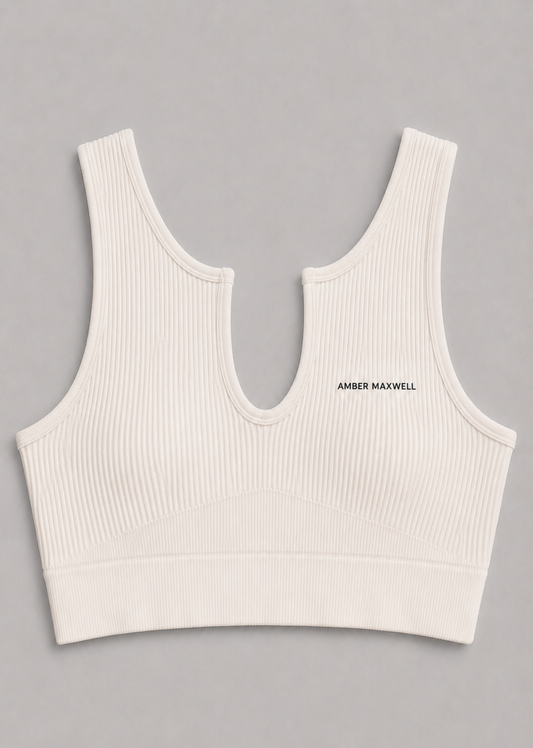 An off-white ribbed knit sports bra with a split neckline and the brand name 'AMBER MAXWELL' printed in black on the left chest, shown flat on a neutral gray background.