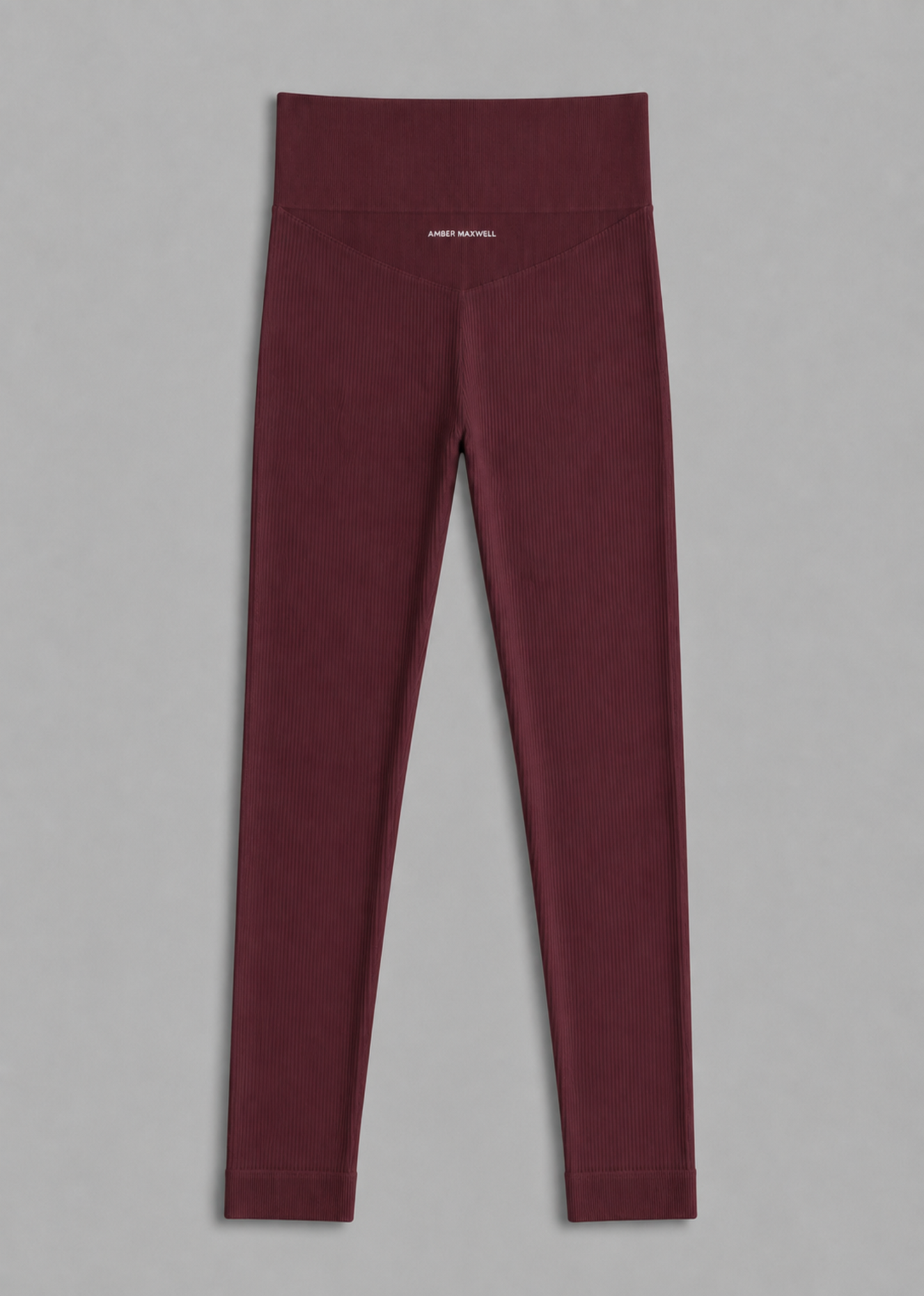A pair of high-waisted burgundy leggings shown flat against a neutral gray background. The brand name 'AMBER MAXWELL' is printed in small white letters on the front center waistband.