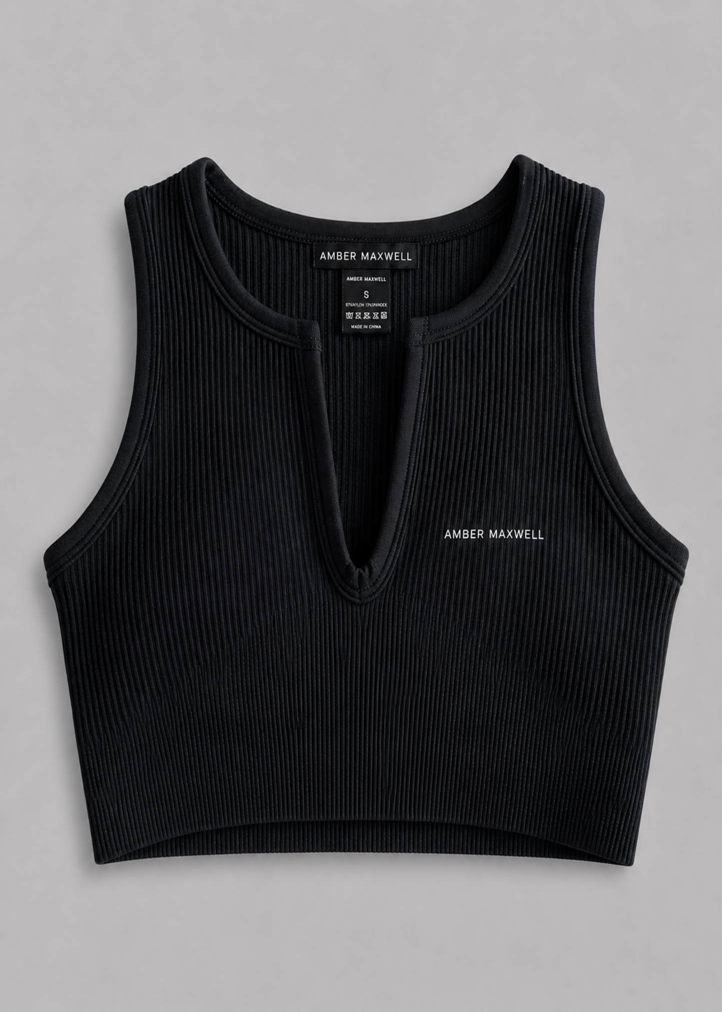 A black ribbed sleeveless crop top with a split neckline and small white embroidered 'AMBER MAXWELL' text on the left chest, shown flat against a neutral gray background.