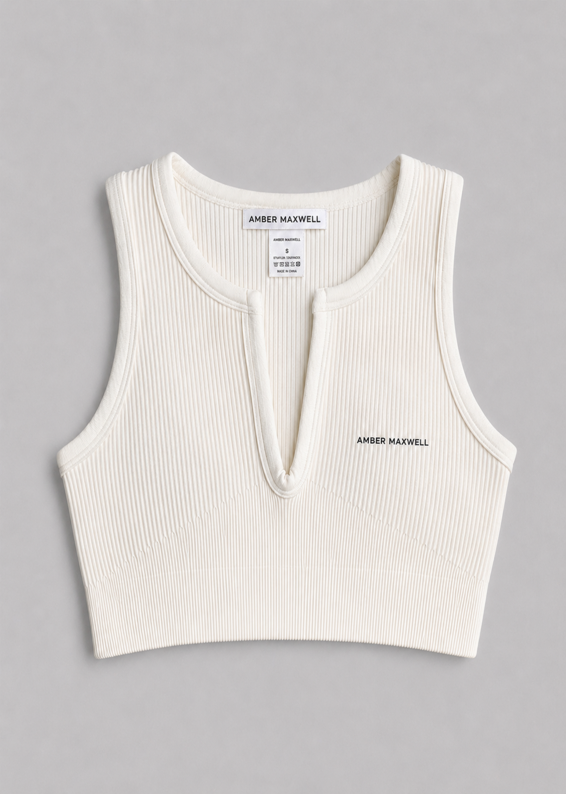 An off-white ribbed knit sleeveless crop top with a split neckline, featuring the brand name 'AMBER MAXWELL' printed on the chest.
