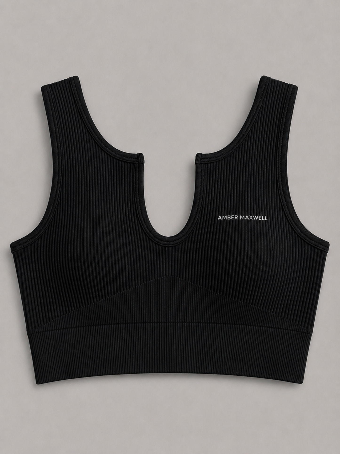 A black ribbed sports bra with a wide underbust band and a small white 'AMBER MAXWELL' logo on the left chest, displayed flat against a neutral gray background.