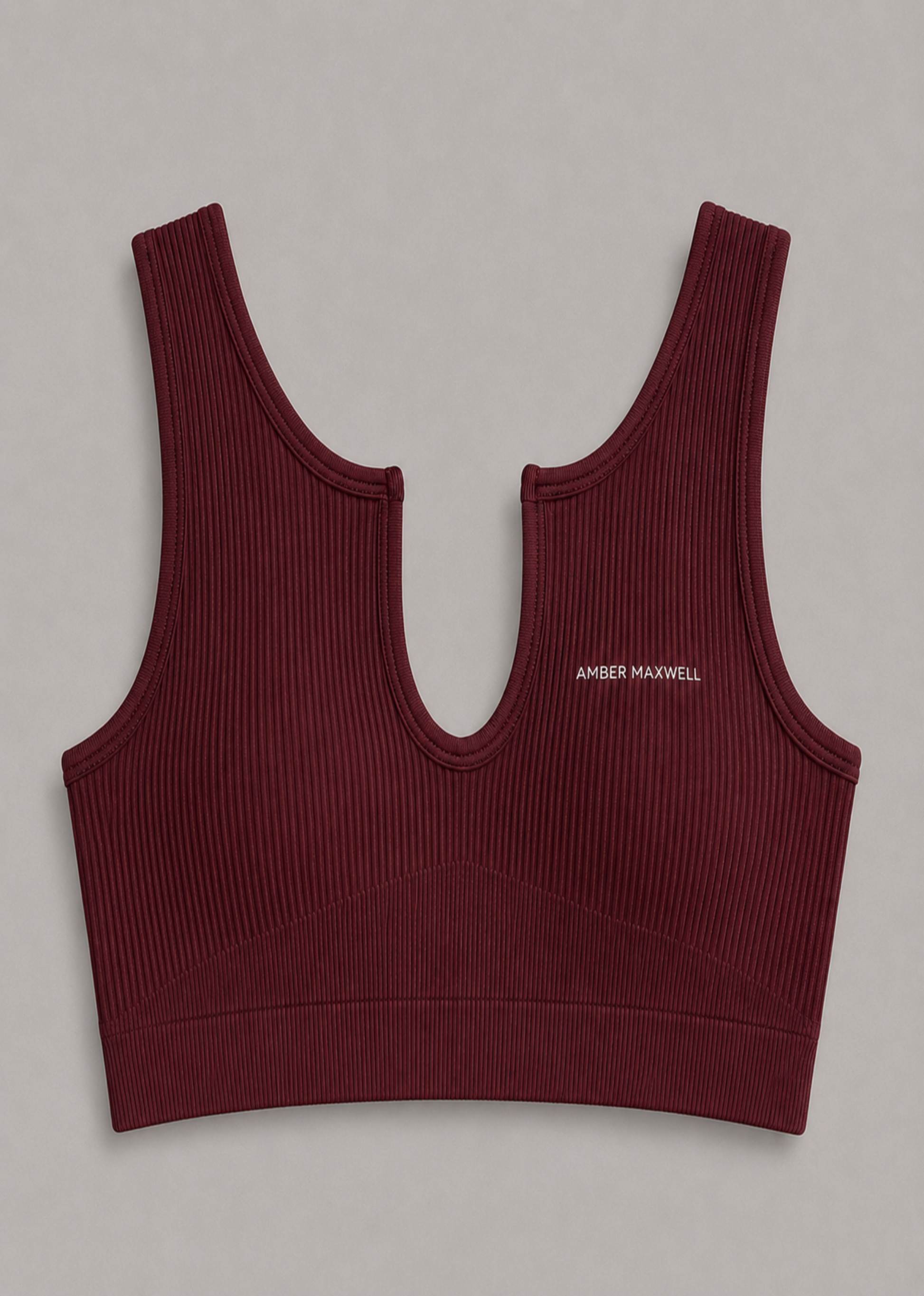 A ribbed knit sports bra in deep burgundy with a small white 'AMBER MAXWELL' logo on the left chest, displayed flat against a neutral gray background.