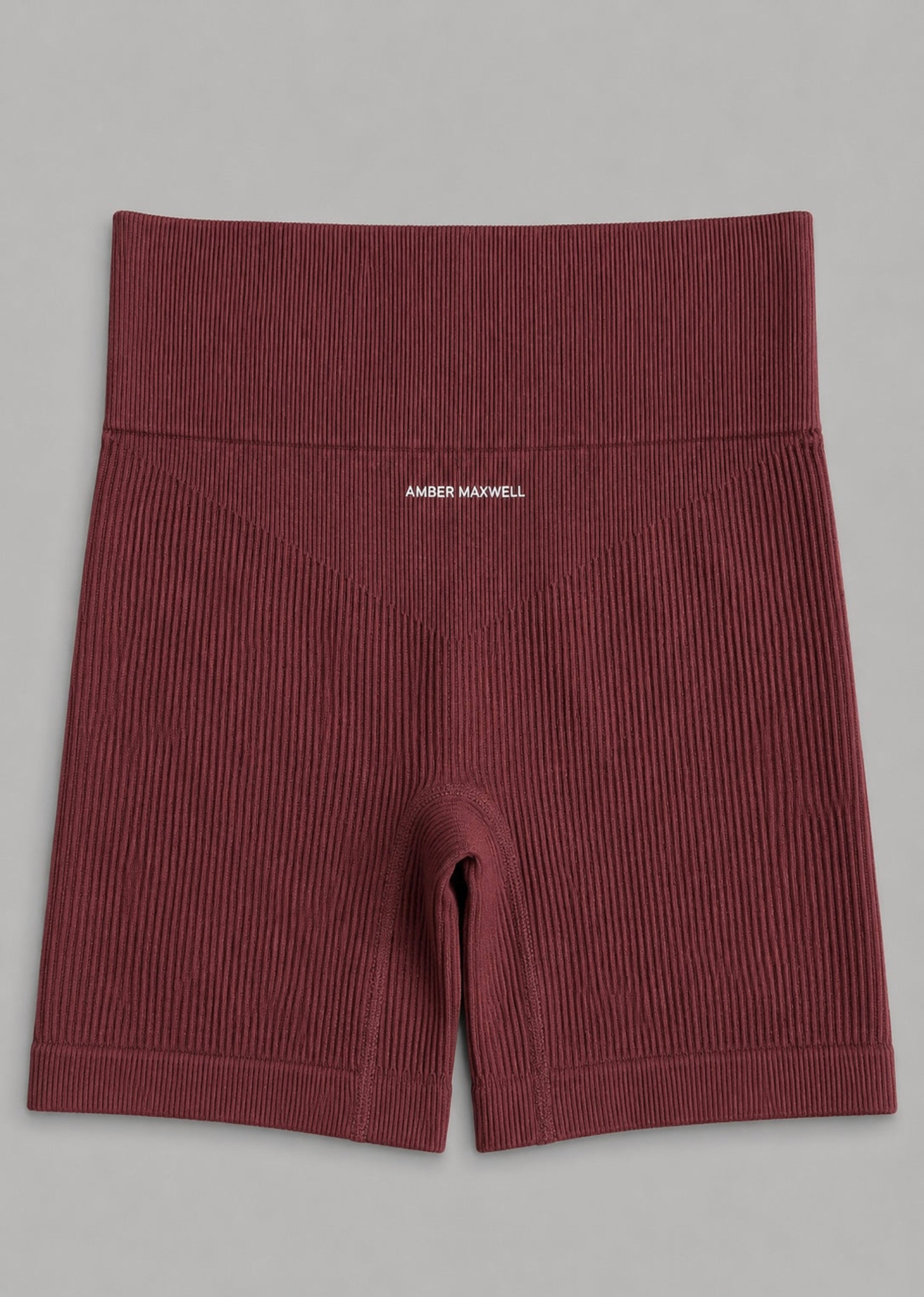 A pair of ribbed knit boxer briefs in a deep burgundy red, featuring a wide elastic waistband with the brand name 'AMBER MAXWELL' printed in white on the front, laid flat on a neutral gray background.