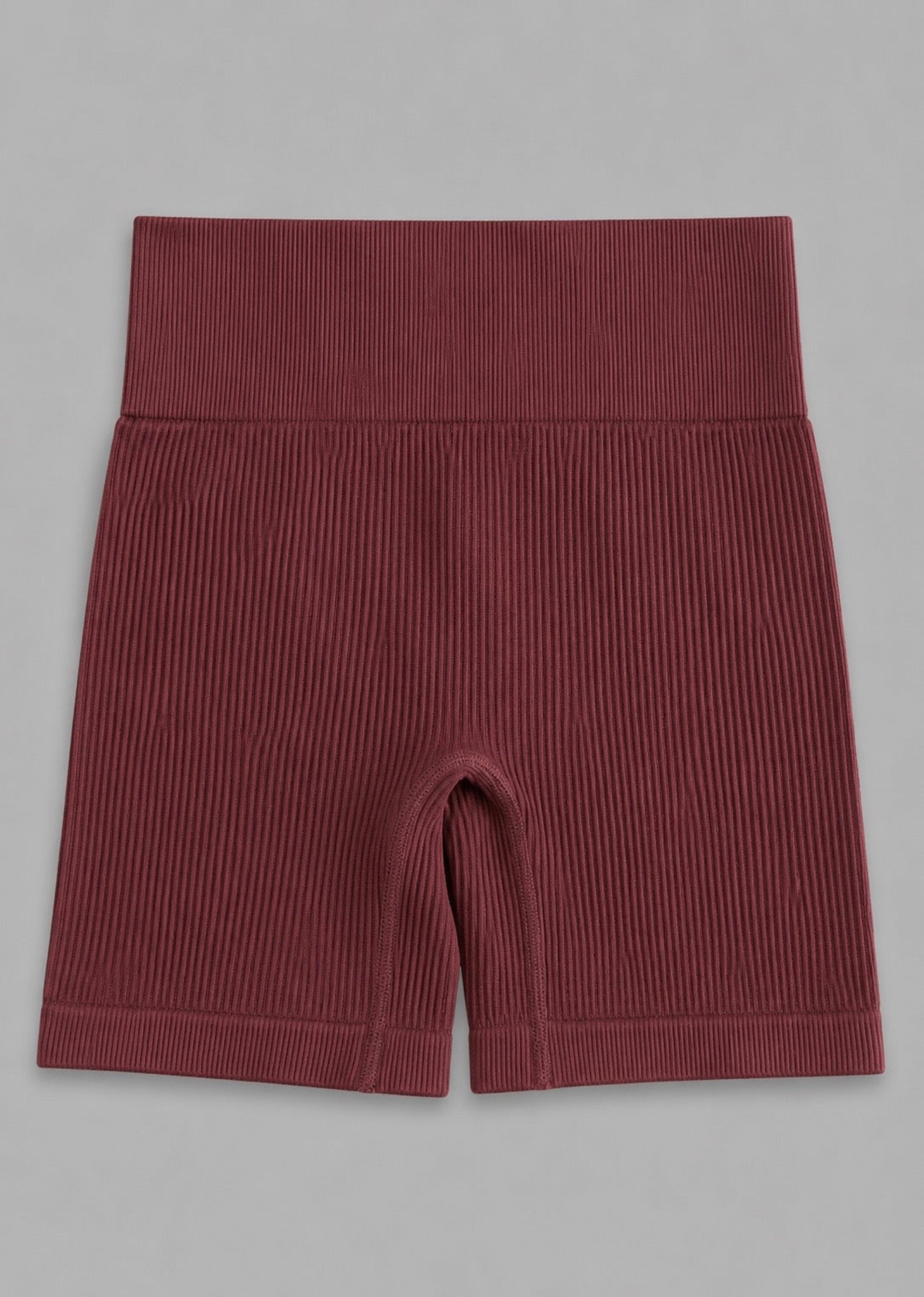 A pair of ribbed high-waisted biker shorts in a deep burgundy red, laid flat against a neutral gray background.